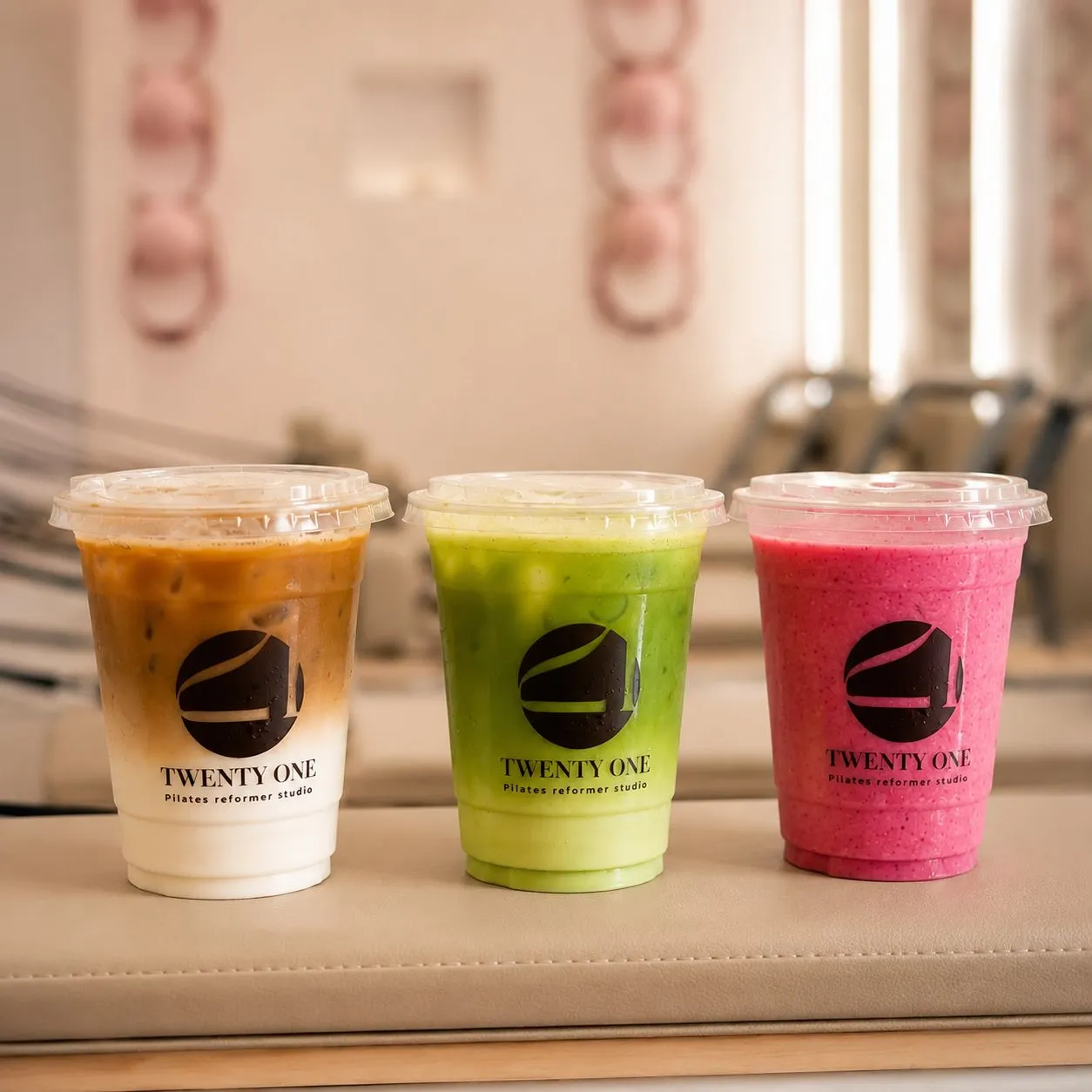Trois boissons glacées aux couleurs du studio, posées sur un reformer : café, matcha, smoothie rose