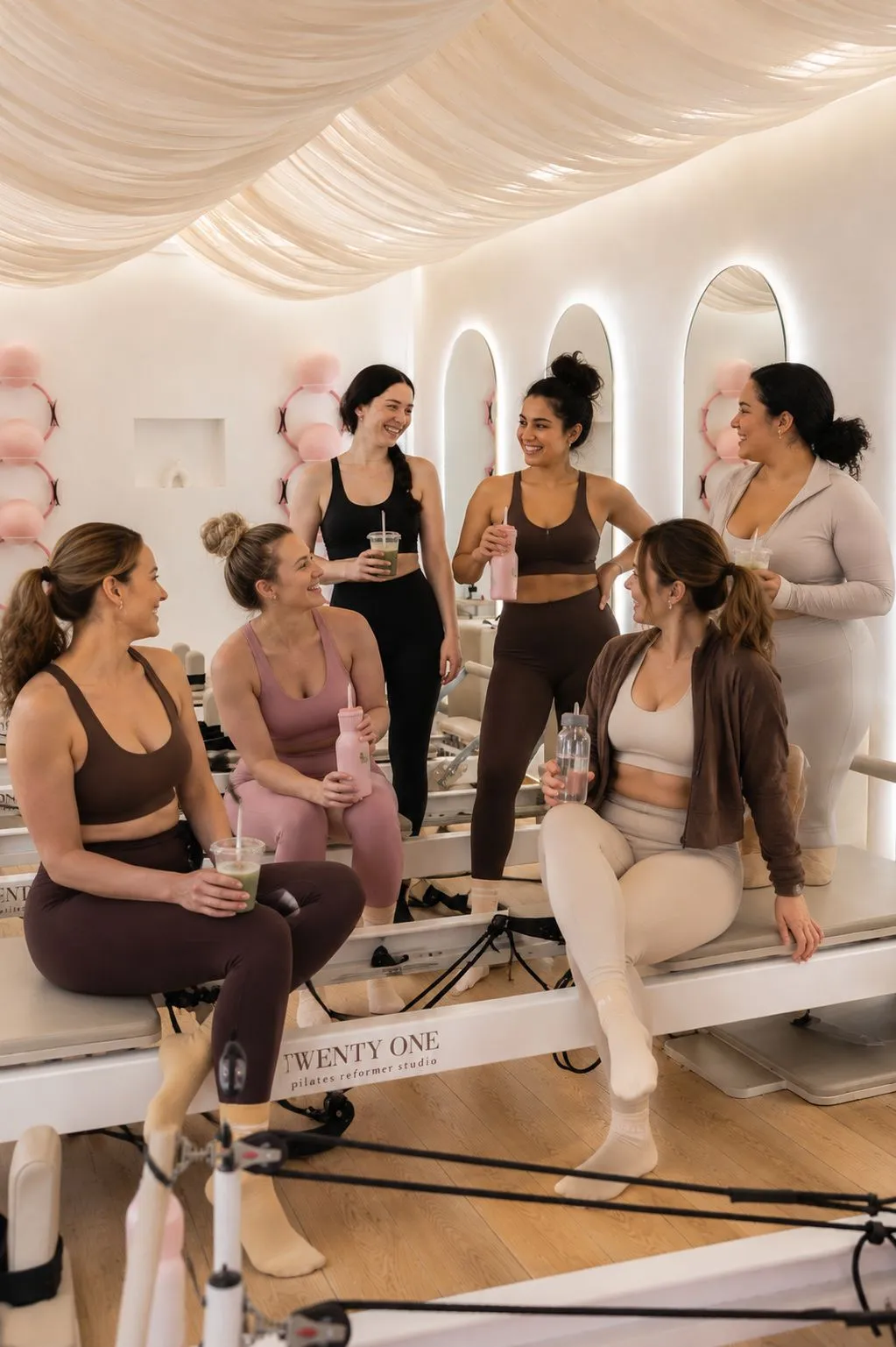 Six femmes en tenue de sport discutent en riant, assises sur les reformers, une boisson à la main