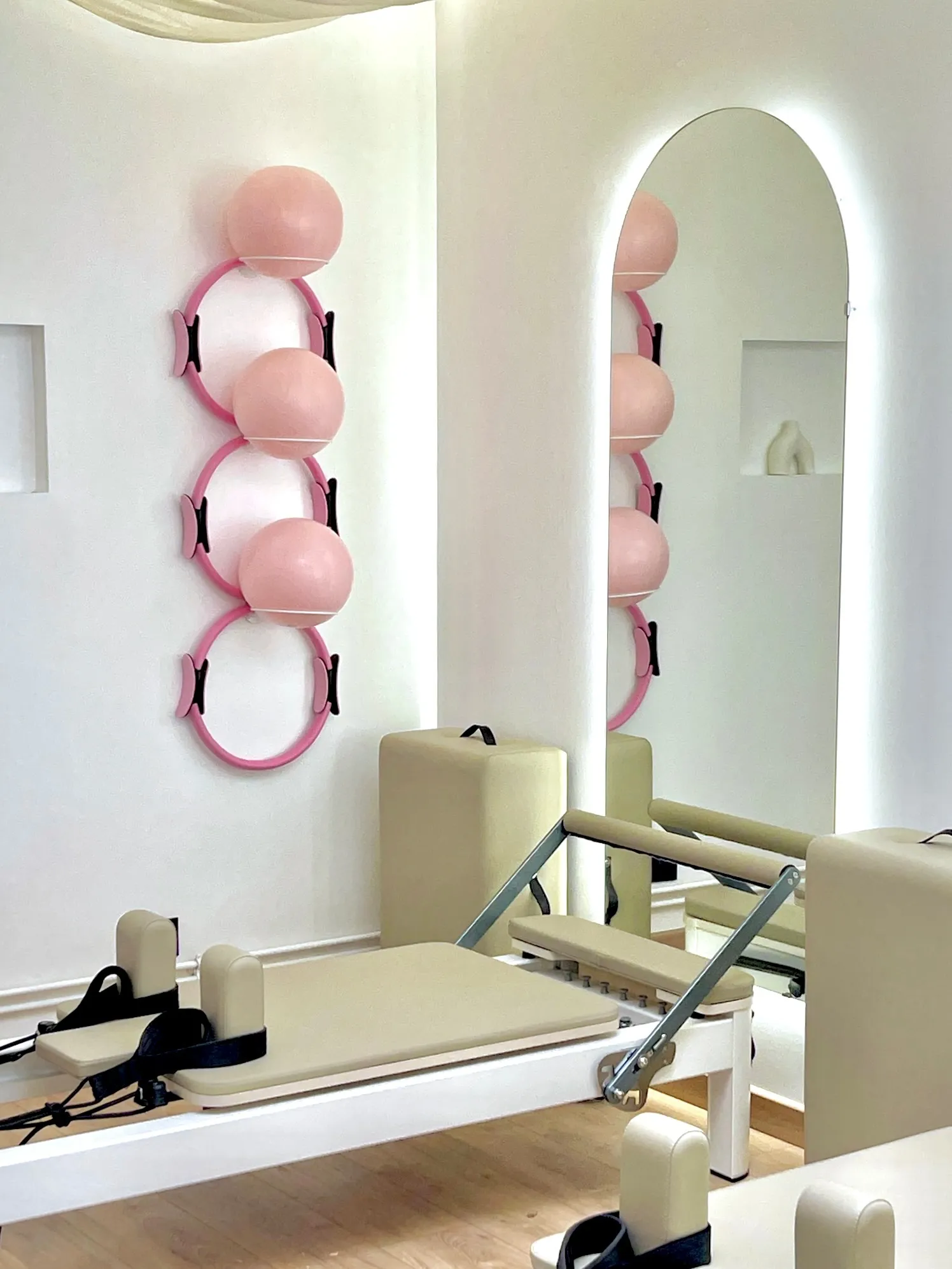 Un reformer devant le mur d’accessoires : ballons et cercles roses, miroir en arche éclairé